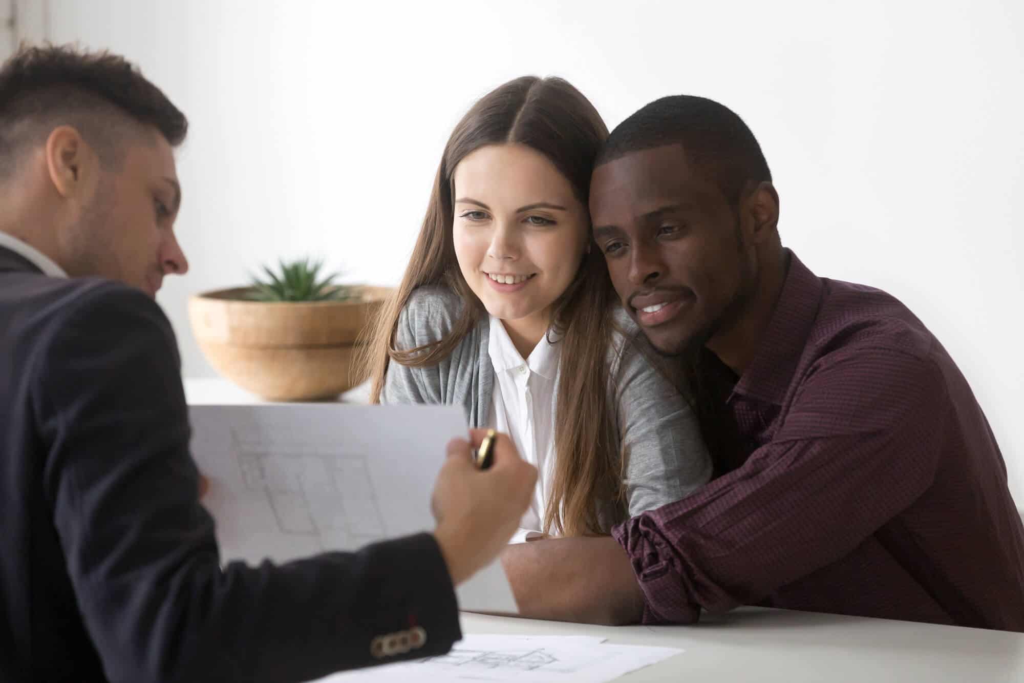 Male real estate agent or consultant showing house plan to happy millennial multiracial couple buying first home together, architect discussing apartment design with spouses or young family